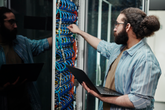 Techniker, der ein Kabel an einen Server anschließt und einen Laptop im Serverraum hält
